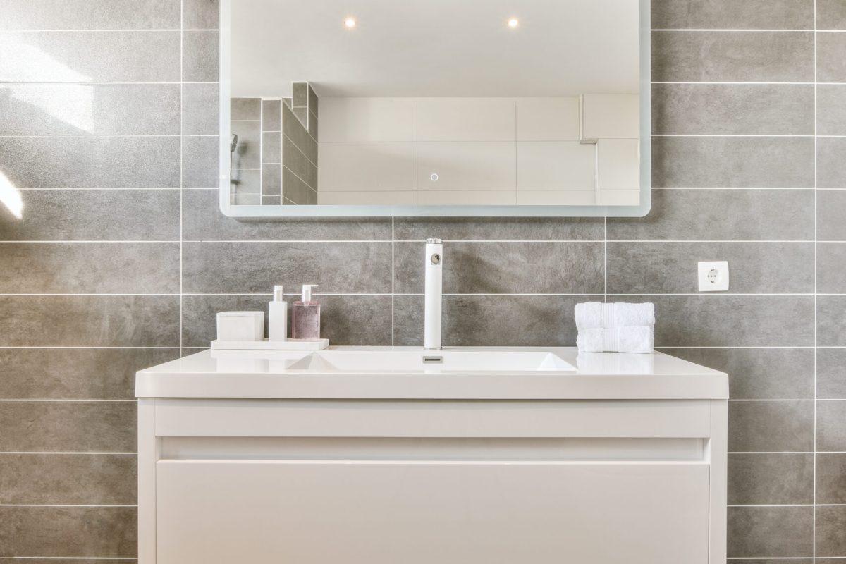 Sink with tap and liquid soap hanging on tiled wall under mirror in contemporary restroom at home